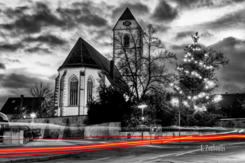 Schwarzweiss-Aufnahme zur Weihnachtszeit in Gärtringen mit der St. Veit Kirche im Hintergrund und einem roten Lichtschweif im Vordergrund