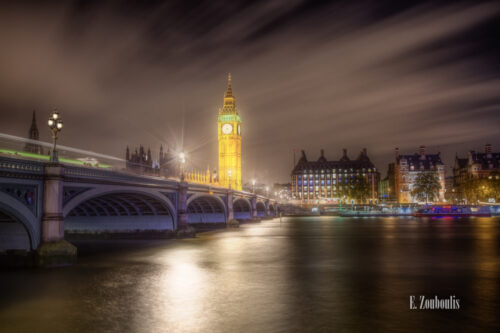 Langzeitbelichtung bei Nacht in London. Die Lichter funkeln und werden von der Themse zum Betrachter hin reflektiert. Im Himmel bewegen sich die Wolken und sorgen in dem Bild, neben den Lichtschweifen auf der Brücke für eine dynamische Komponente