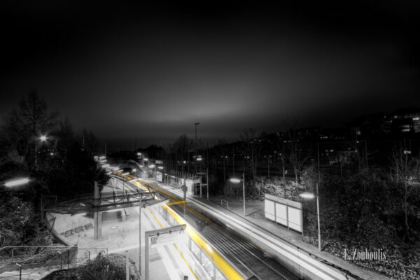 Schwarzweiß-Aufnahme am Herderplatz in Stuttgart. Eine Geister - Straßenbahn hinterlässt einen gelben Lichtschweif