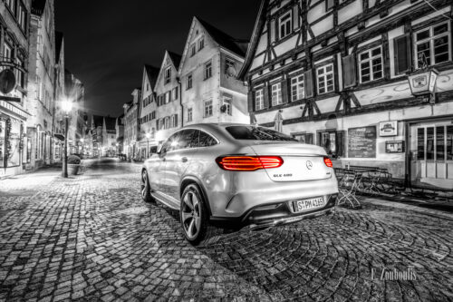 Schwarzweiß Aufnahme in der Altstadt von Esslingen. Im Vordergrund ein Mercedes GLE mit roten Heckleuchten auf einer gepflasterten Straße vor schönen Fachwerkhäusern