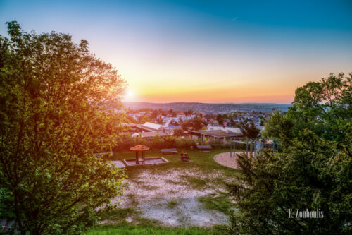 Abendliche Aufnahme zum Sonnenuntergang an der Geroksruhe in Stuttgart mit Blick auf die Innenstadt. Im Vordergrund der Spielplatz und Bäume. Im Hintergrund die Dächer von Stuttgart, die durch die tiefstehende Sonne leuchten