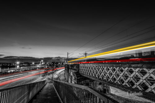 Blick hinunter auf die Pointhouse Road in Glasgow. Links ist der River Clyde zu sehen und rote Lichtschweife des vorbeiziehenden Verkehrs. Auf der rechten Seite führ ein Zug über die Brücke und hinterlässt gelbe und rote Lichtschweife