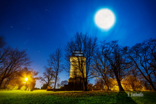 Nachtaufnahme am Bismarckturm in Stuttgart-West bei Vollmond. Im Vordergrund das Gras und gefallene Blätter. im Hintergrund der Bismarckturm, der vom Mond angeleuchtet wird