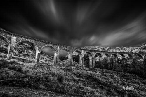 Schwarzweiß-Aufnahme mit einer Langzeitbelichtung, die die Wolken in Ihrer Bewegung sichtbar macht. In der Mitte des Bildes befindet sich das Glenfinnan Viadukt welches als "Harry Potter Bridge" aus den Filmen bekannt wurde